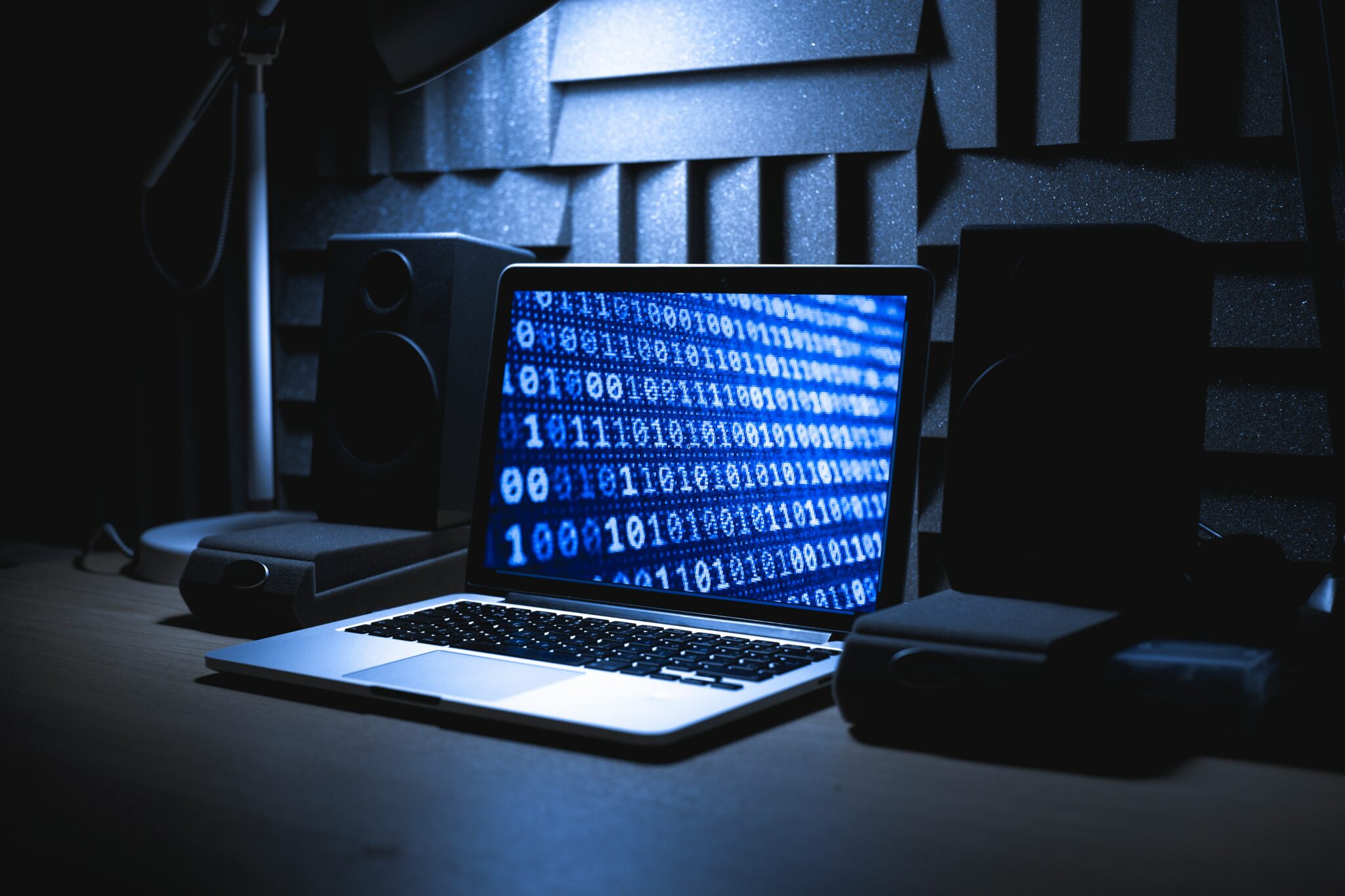 computer displaying binary code, flanked by speakers in a soundproof room